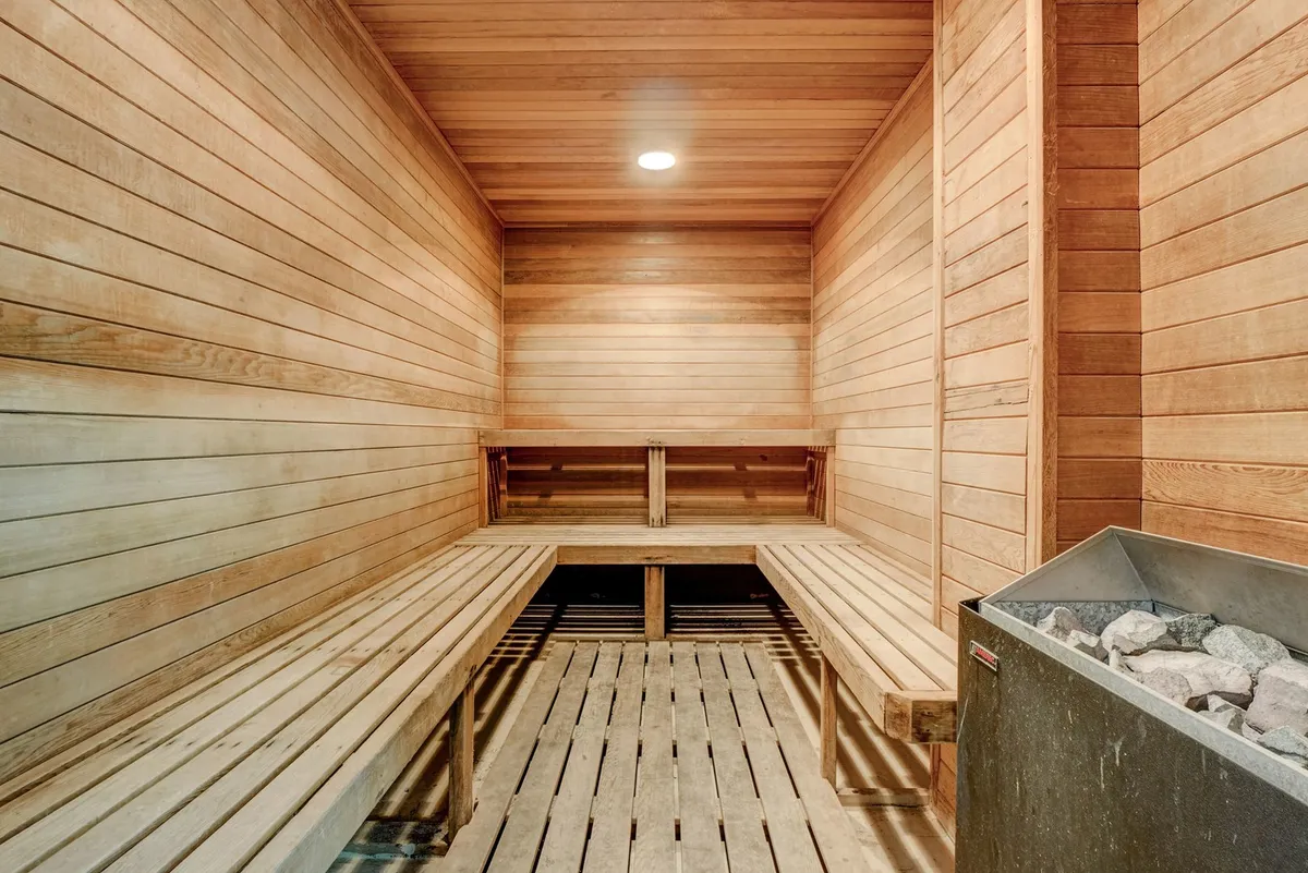 A serene sauna area is depicted, with wooden seating benches and a central stone heater. The ambiance is tranquil and inviting, encouraging relaxation and moments of peace after a workout or an active day.