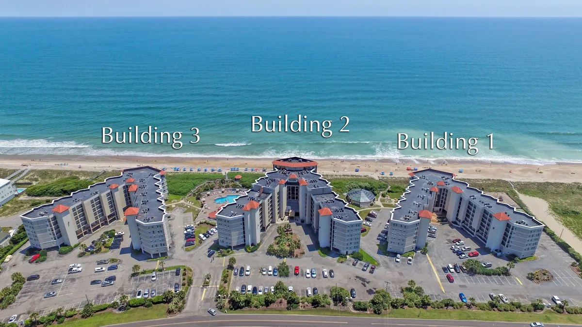 This exterior image features the St. Regis Resort beachfront with three prominent buildings, a sparkling swimming pool, and direct access to the sandy beach. The pool is expansive and inviting, surrounded by plenty of space for lounging and social activities. The view suggests a lively yet relaxing atmosphere where resort guests can enjoy both water recreation and the natural beauty of the oceanfront setting.