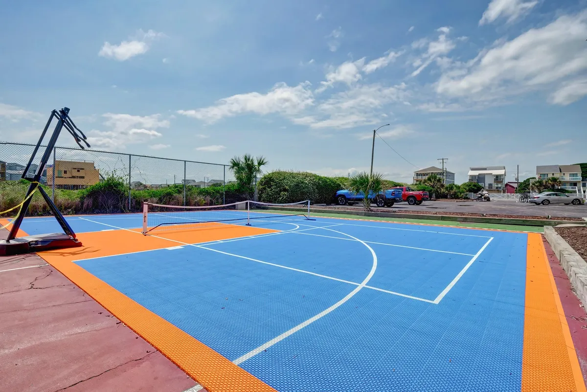 An outdoor multi-purpose court featuring a basketball hoop and tennis net with a colorful, well-maintained surface. The space is designed for energetic games, group activities, and friendly competition.