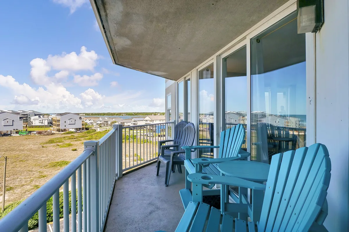 A tranquil view from a seaside balcony with bright blue chairs overlooking the ocean and nearby homes. The open vista captures the promise of sunrise walks, the gentle sounds of the waves, and peaceful moments spent simply enjoying the view from a private perch.