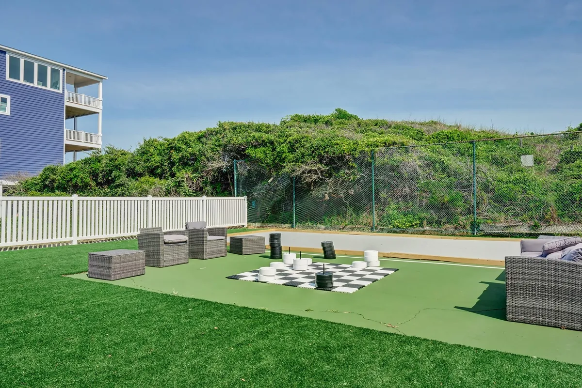 An exterior scene featuring an oversized chessboard set on green grass, surrounded by comfortable lounge seating. The outdoor setting is perfect for socializing, playing games, or enjoying sunny afternoons with friends and family.