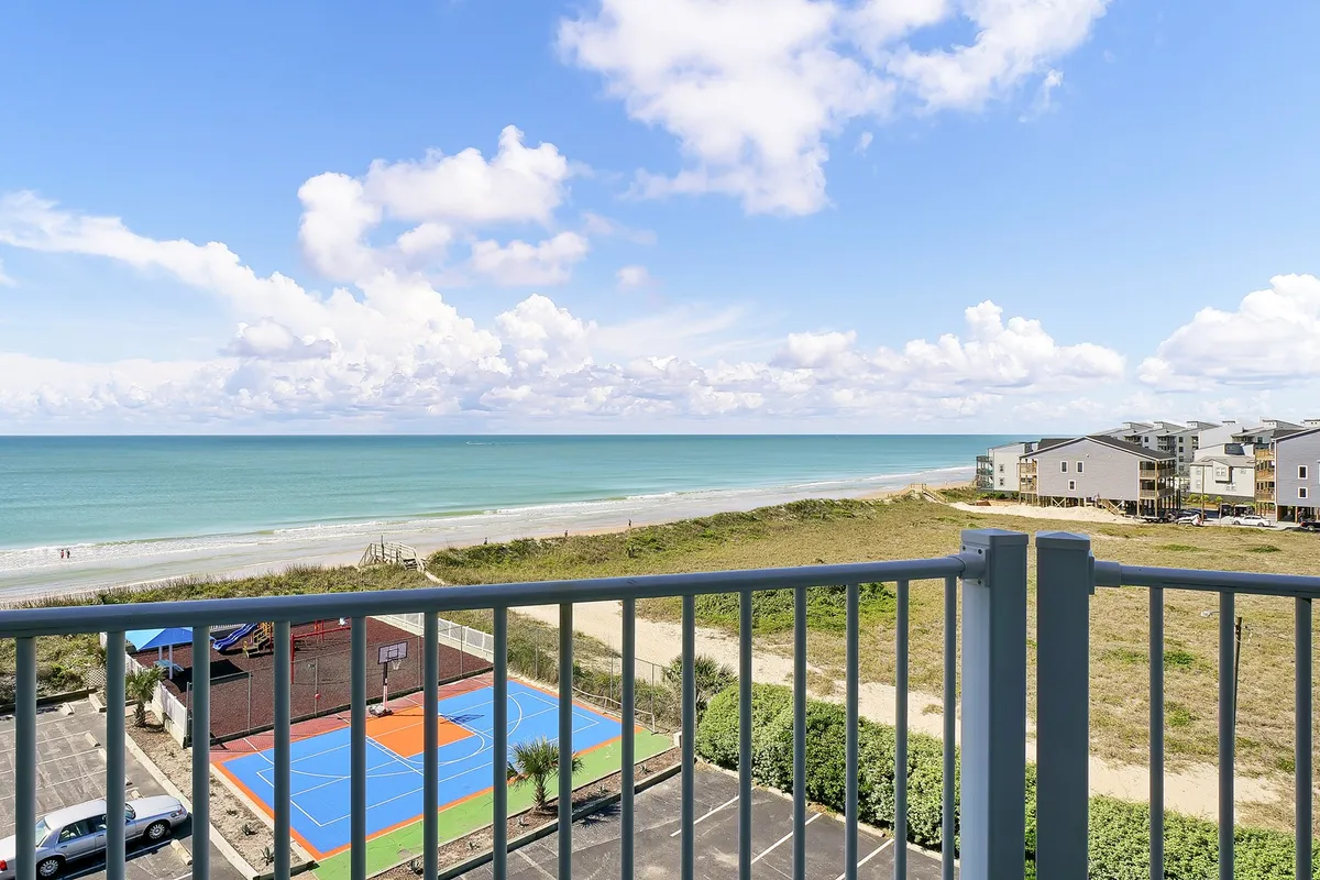 The hero image showcases a stunning ocean view at North Topsail Beach, with the sun rising over the water. In the foreground, there's a basketball court inviting friendly games, and the scene hints at beachside activities and relaxation on a balcony. The overall mood is inviting and vibrant, with a spectacular natural backdrop.