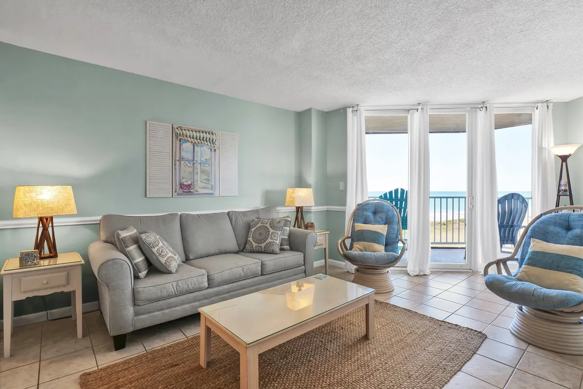 A comfortable gray sofa faces colorful accent chairs and a modern coffee table, with an expansive ocean view through large windows. The layout invites both relaxation and group conversation, with natural light enhancing the welcoming mood.