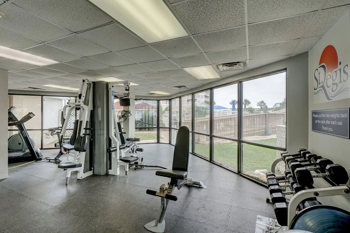 This image showcases a bright, modern fitness area filled with exercise equipment, large windows letting in natural light, and motivational signage on the walls. Cardio machines and fitness spaces are visible, creating an energetic atmosphere ideal for workouts and personal training sessions.