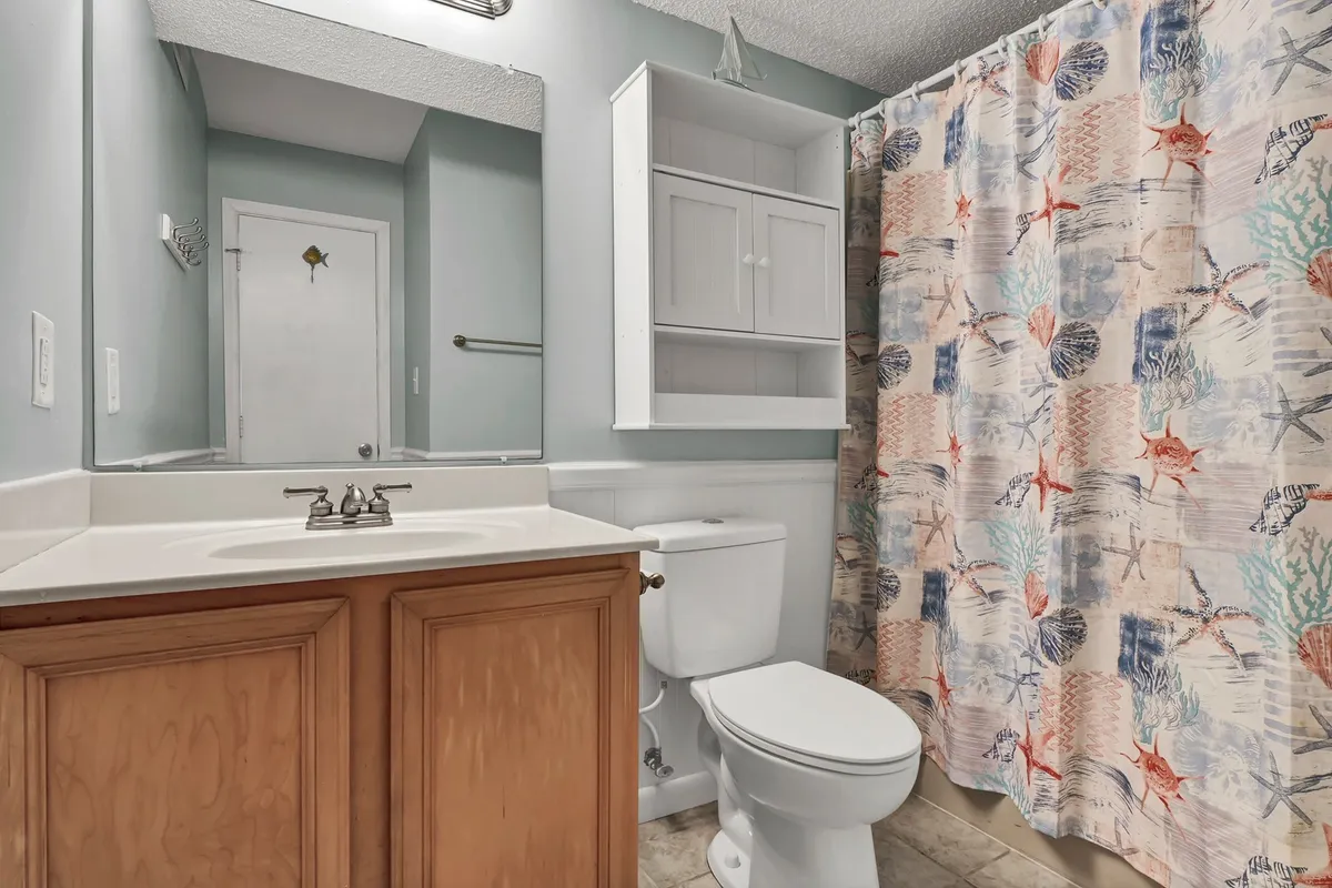 A bathroom with a modern vanity, bright mirror, and a colorful shower curtain. The space is refreshed by natural light and offers an inviting, clean environment for personal routines.