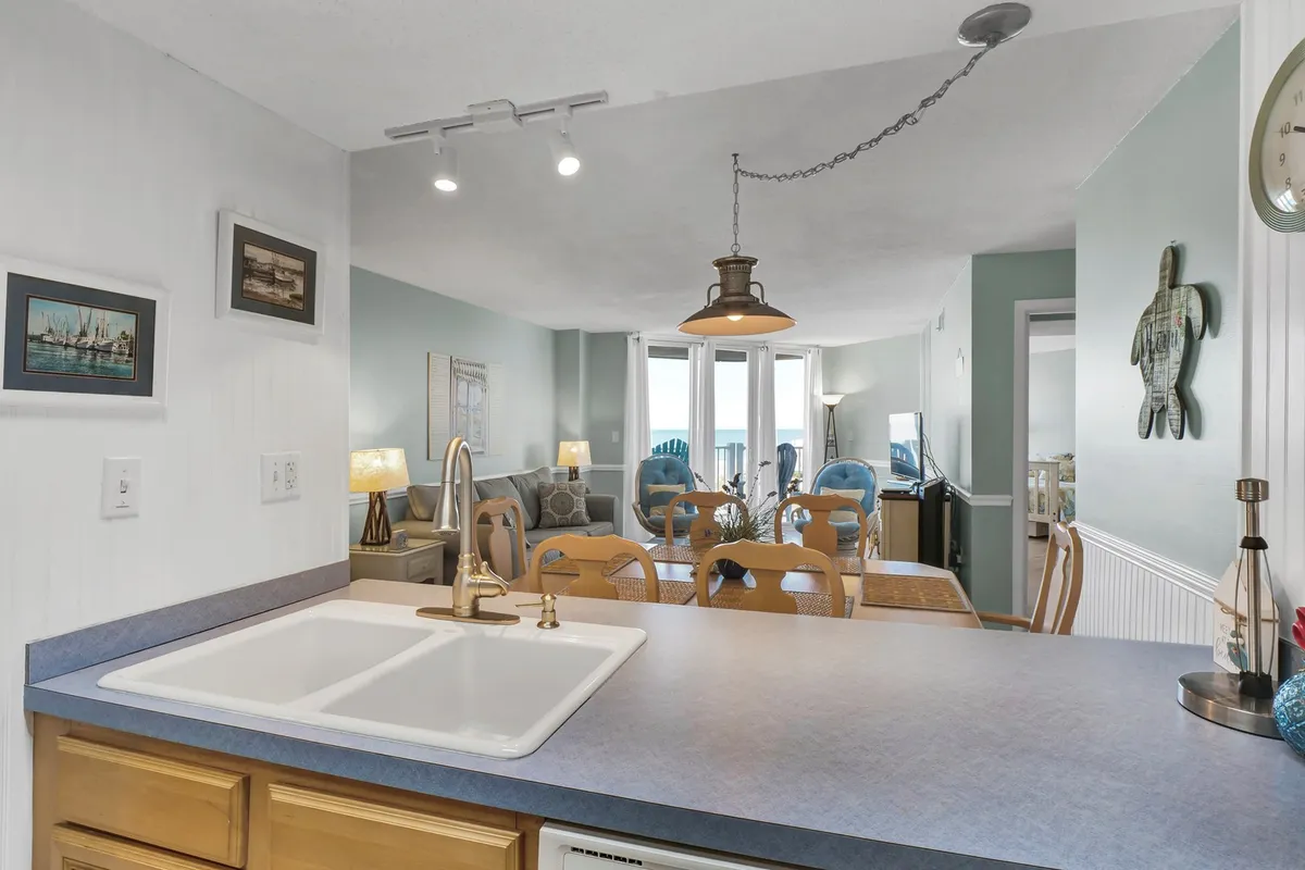 Taken from a different vantage point, this image looks over the kitchen sink toward the dining table and out into the living area. The new hardwood floors gleam in the sunlight, and the space feels open and inviting. The arrangement encourages social interaction, whether it's preparing a meal, sharing a family dinner, or playing a board game at the table.