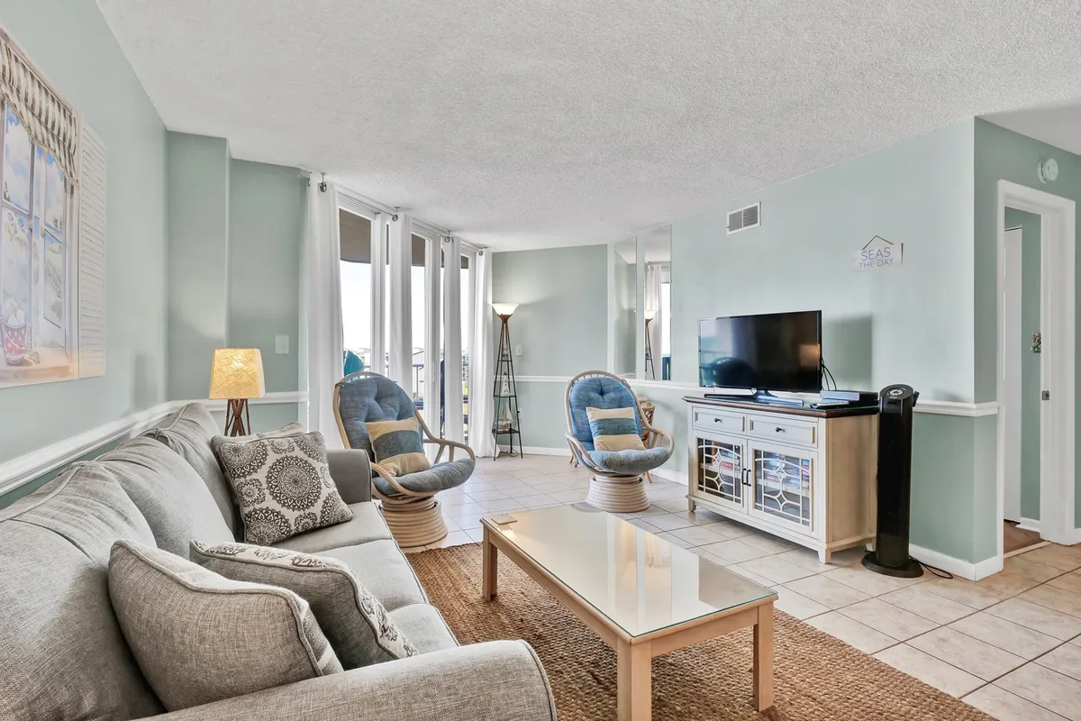 A casual, comfortable living area with a cozy sofa, blue accent chairs, a coffee table, and a television. Sunlight spills in, creating an inviting space for relaxation, socializing, or quiet afternoons.